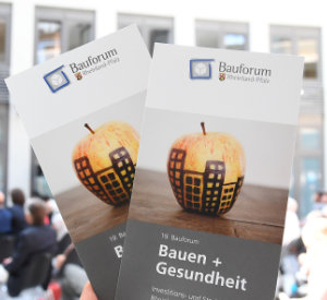 Flyer des Bauforums Rheinland-Pfalz zum Thema Bauen und Gesundheit. Es ist ein Apfel mit Bemalung einer Häuserzeile auf dem Cover.