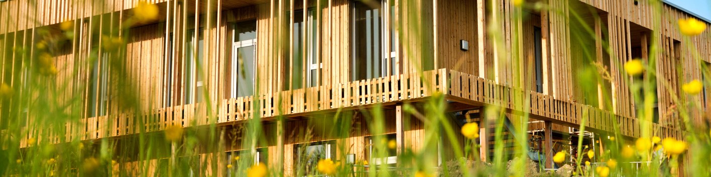 Holzhaus mit durchlaufendem Holzbalkon und grüner Wiese im Vordergrund
