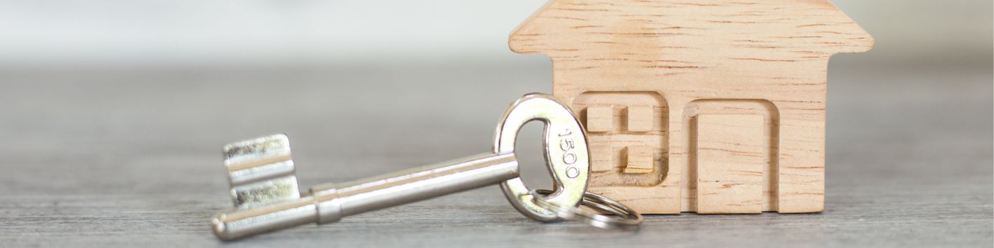 Ein Spielzeughaus aus Holz mit einem Schlüssel aus Metall davor.