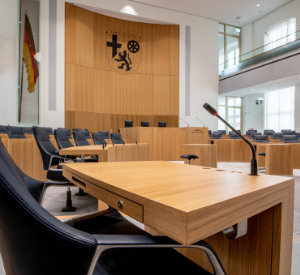Plenarsaal des rheinland-pfälzischen Landtags. Fokus liegt auf dem Landeswappen neben der Deutschlandfahne. 