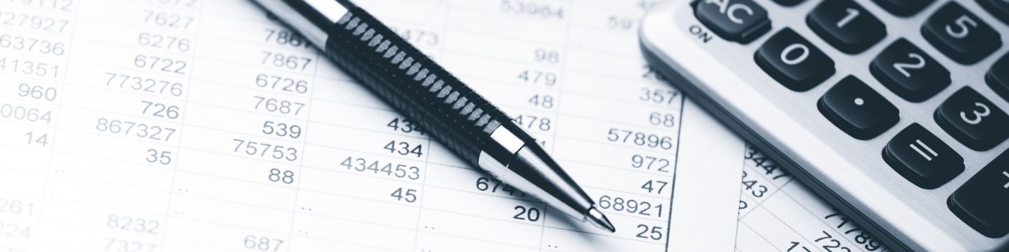 Ein Kugelschreiber sowie ein Taschenrechner liegen auf Papieren, die mit Zahlen bedruckt sind.