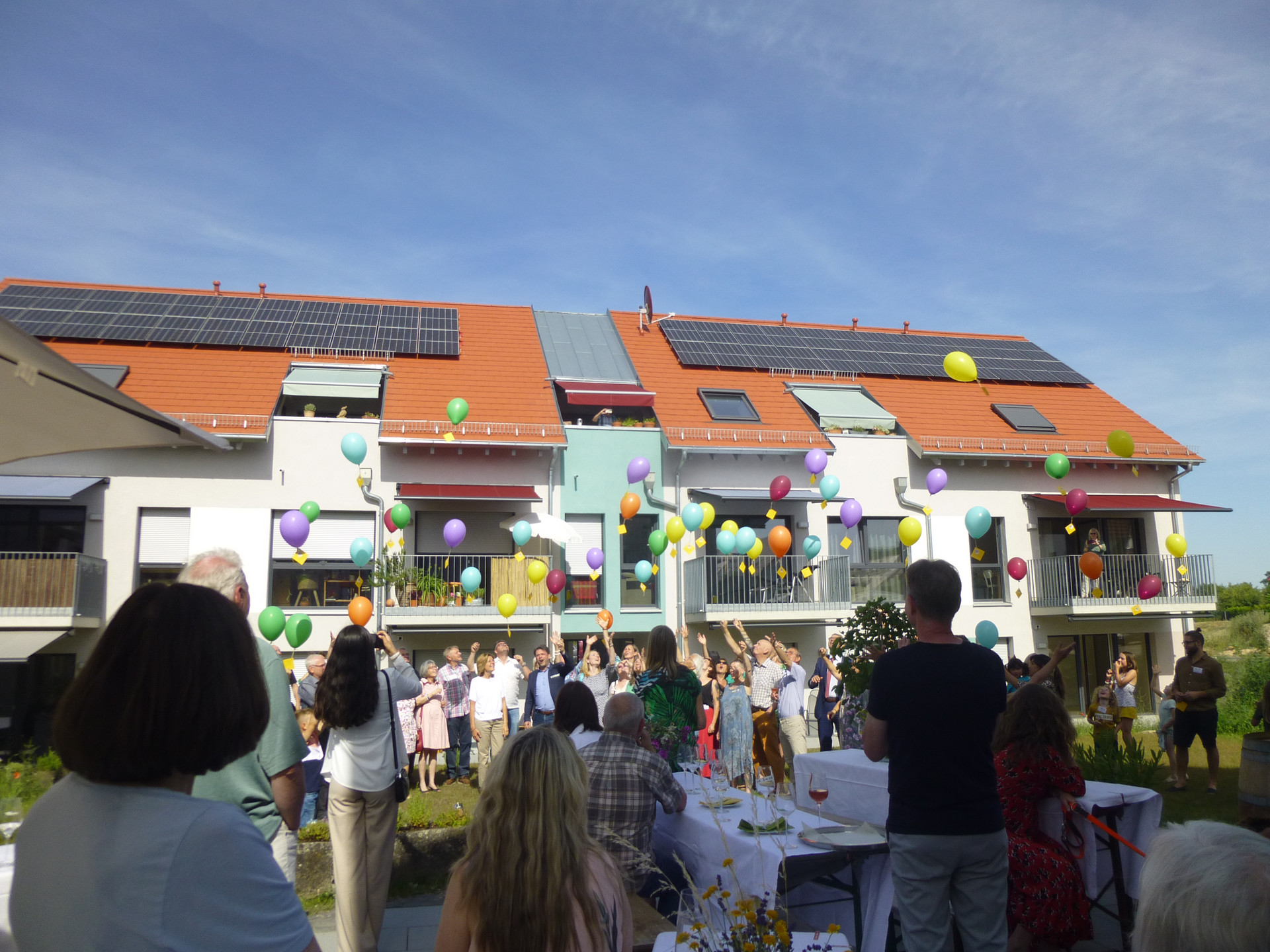Wohngebäude mit Menschen im Vordergrund, die Luftballons steigen lassen