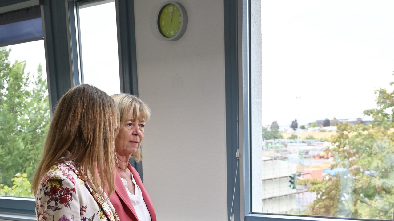 Zwei Frauen stehen vor Stühlen auf denen Schutzwesten liegen.