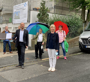 Viele Menschen stehen auf der Straße vor einer Baustelle. 