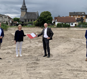 Eine Gruppe von vier Personen steht auf einer Baustelle. Die Frau in der Mitte und der Mann in der Mitte halten eine Mappe mit einem Förderbescheid nach oben.