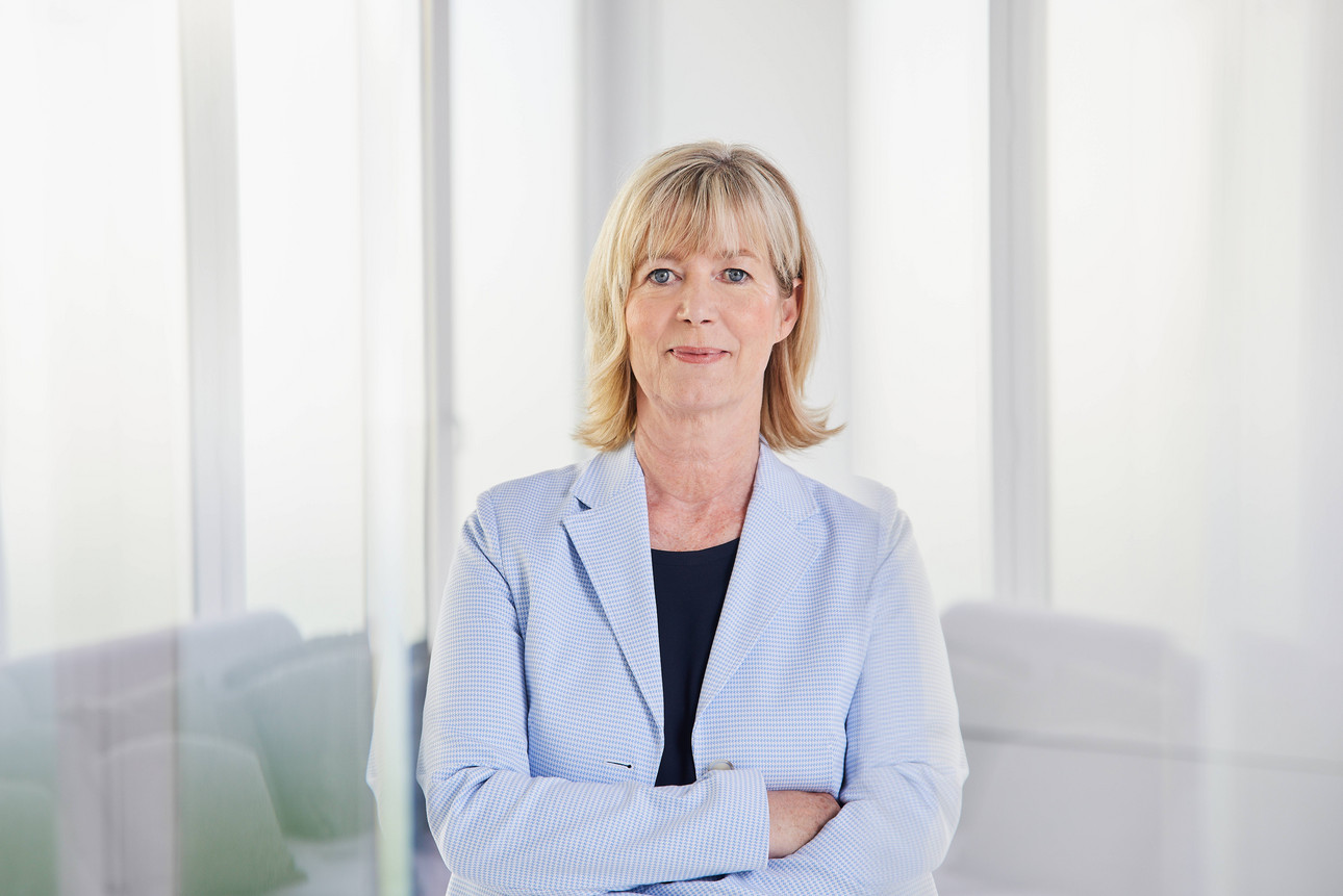 Eine Frau steht mit verschränkten Armen da. Sie lächelt in die Kamera und trägt ein T-Shirt mit einem Blazer. 