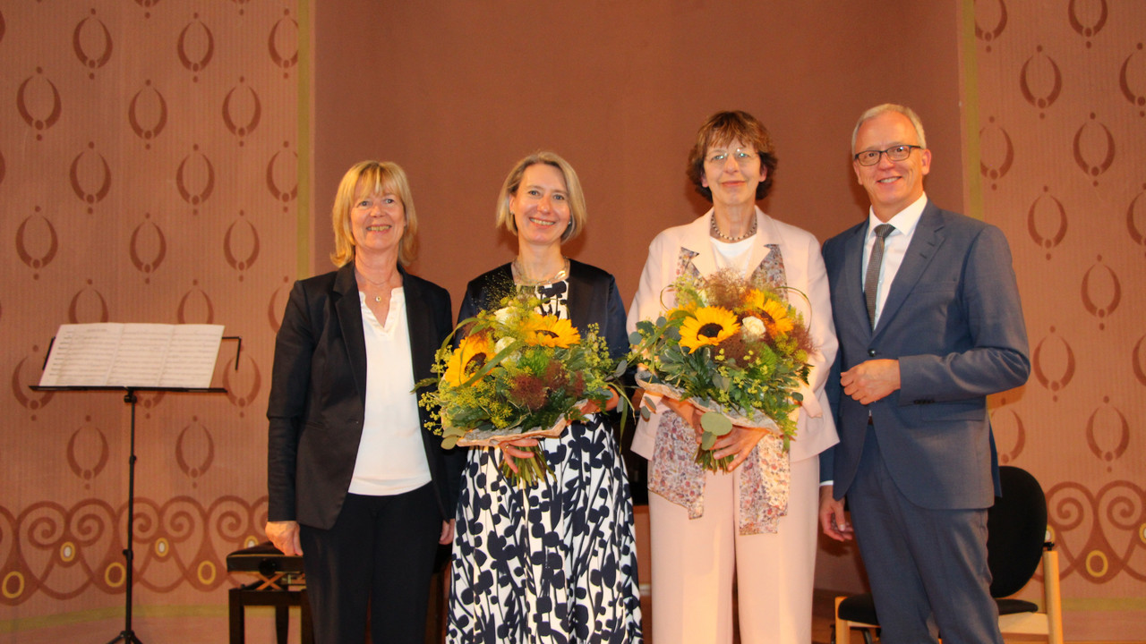 Eine Gruppe von vier Personen lacht in die Kamera. Die zwei Frauen in der Mitte halten einen Blumenstrauß in der Hand.