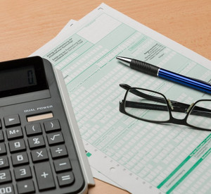Ein Taschenrechner, ein Kugelschreiber und eine Brille liegen auf einem Formular, das zur Steuererklärung genutzt wird.