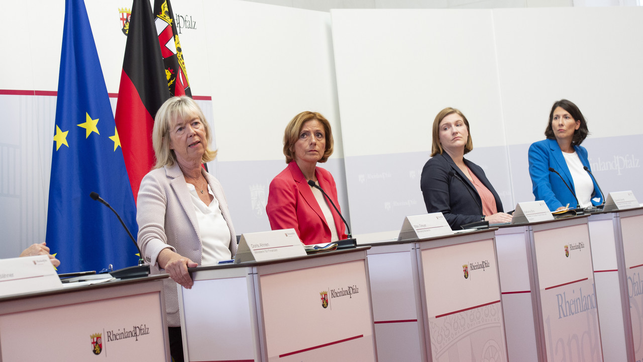 Vier Frauen stehen hinter Rednerpulten. Sie blicken auf die Personen vor sich. Hinter ihnen sind drei Flaggen zu erkennen.