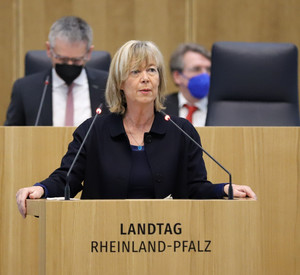 Eine Frau steht an einem Redenpult mit einem Mikrofon und schaut in die Menge.