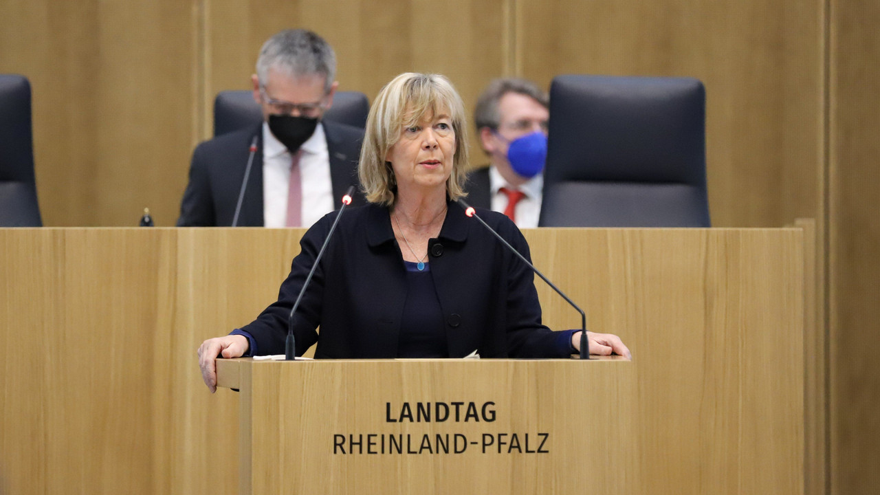 Eine Frau steht an einem Redenpult mit einem Mikrofon und schaut in die Menge.