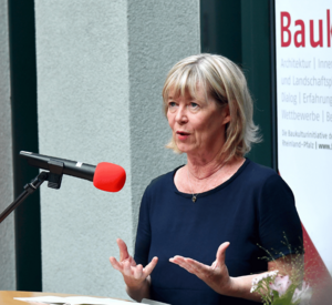 Eine Frau spricht an einem Stehpult in ein Mikrofon.